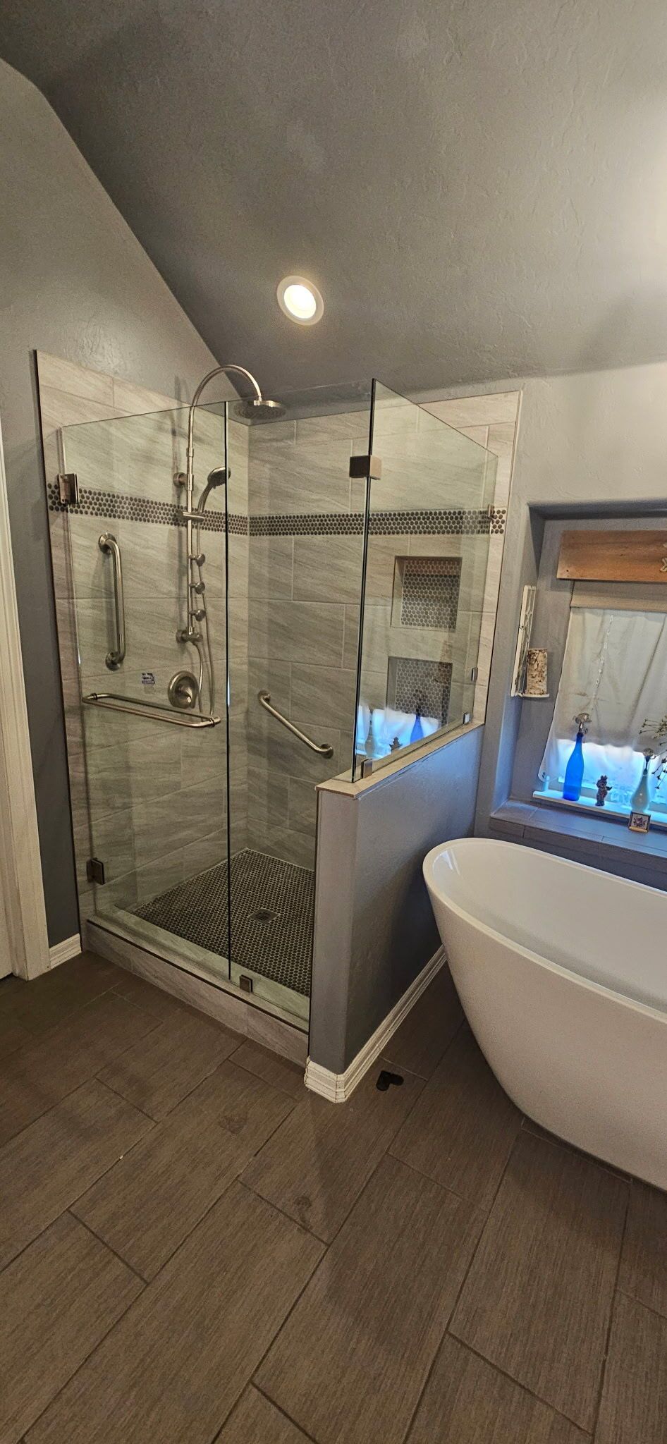 Modern bathroom with glass shower, toilet, and freestanding tub beside a window