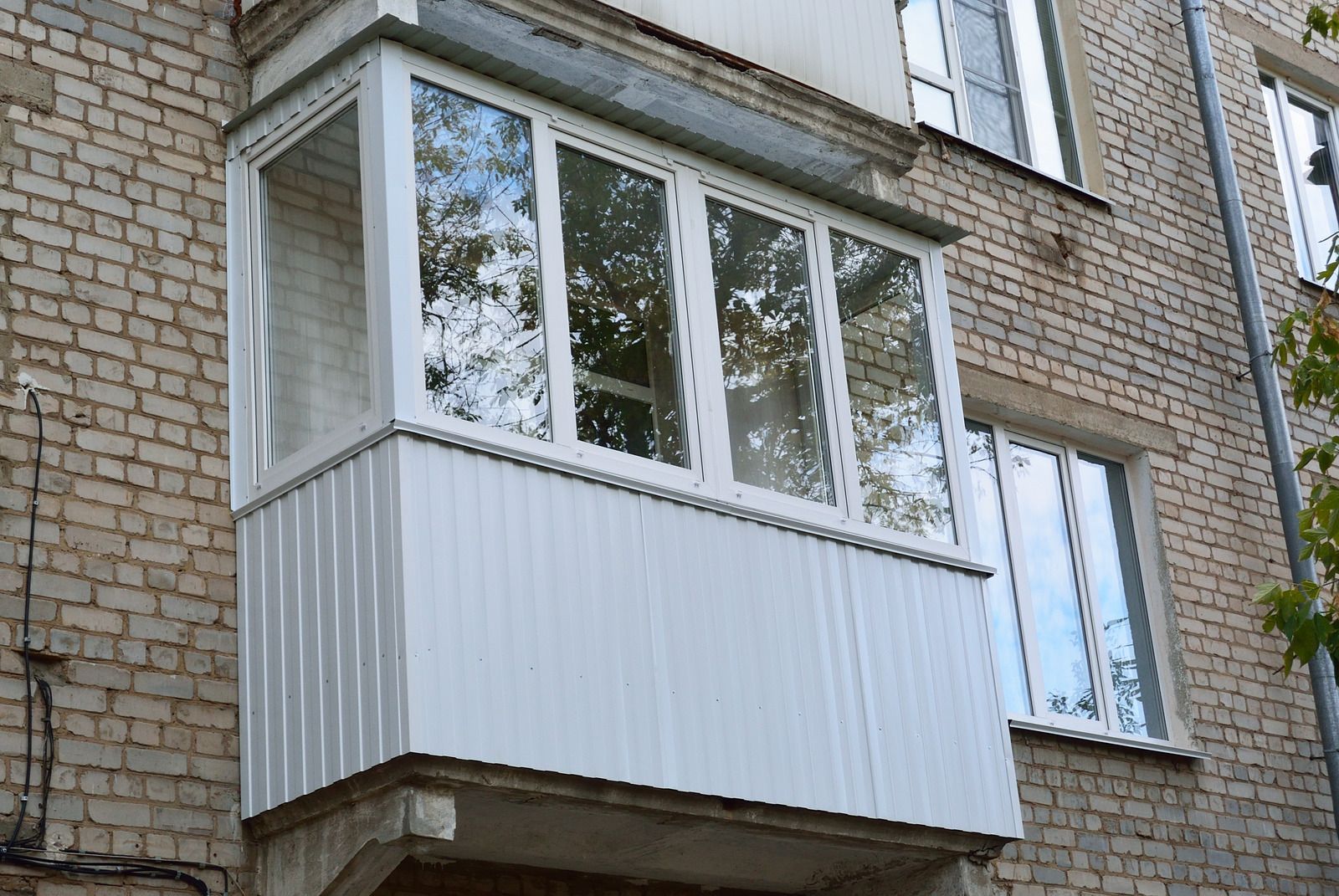 Enclosed balcony with white windows and paneling on a brick apartment building