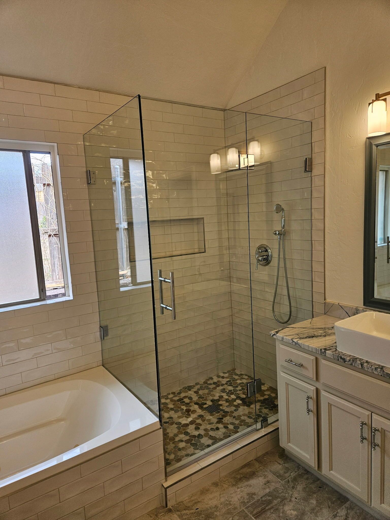 Modern bathroom with a glass walk-in shower, bathtub, and vanity with mirror lights.