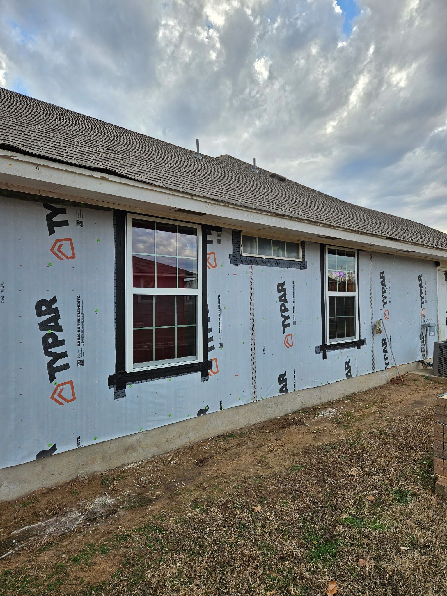 House exterior under construction with white house wrap, windows, and a shingled roof.