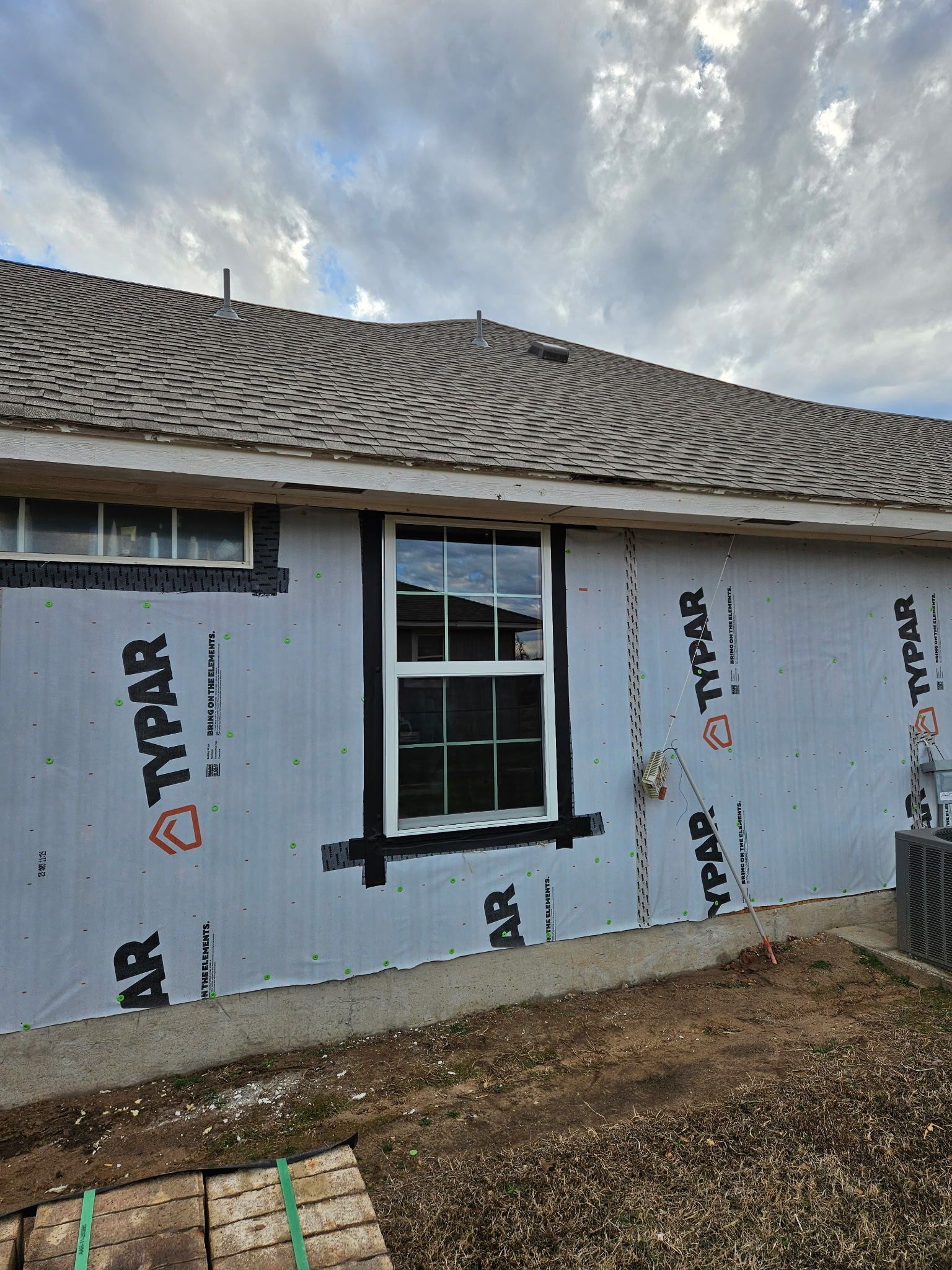 House exterior with white wrap, two windows, and a tiled roof under a cloudy sky