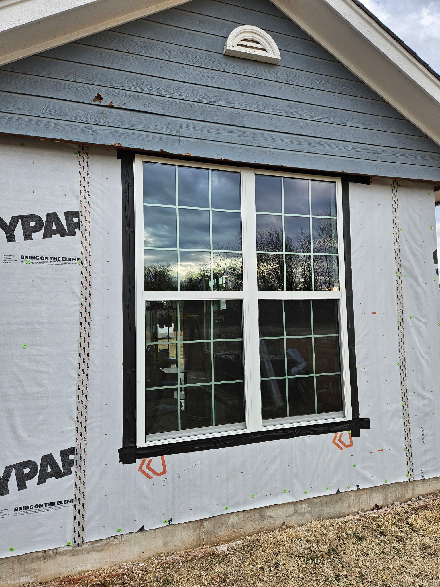 New window installed in gray house wall with black trim and white protective wrap