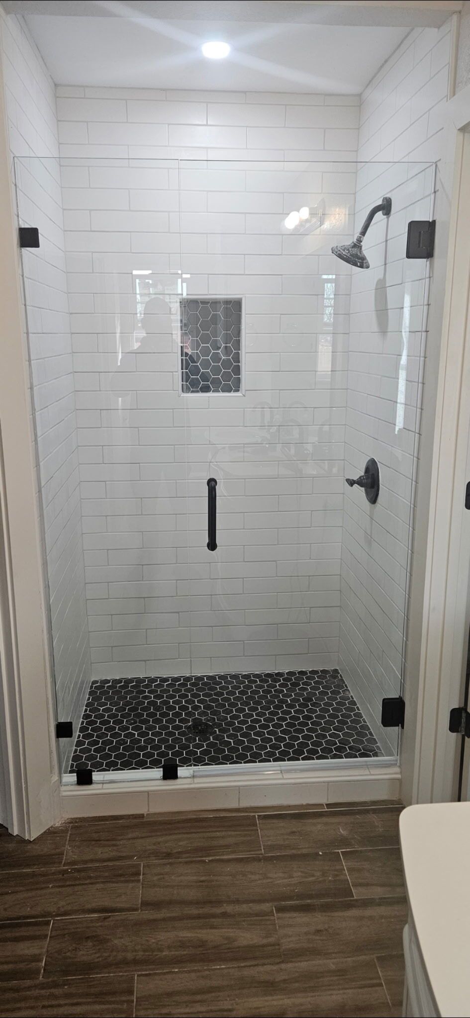 Modern white-tiled walk-in shower with black mosaic floor and chrome fixtures, viewed from outside the bathroom door