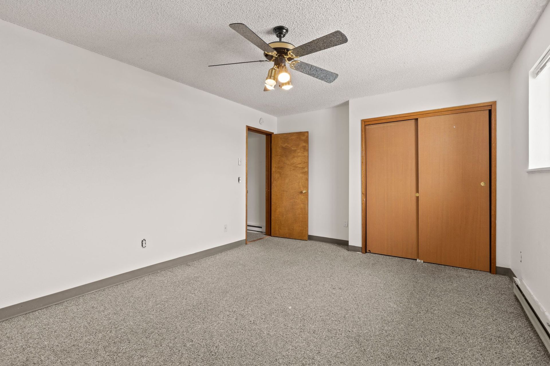 Empty bedroom with gray carpet, white walls, closet, and ceiling fan.