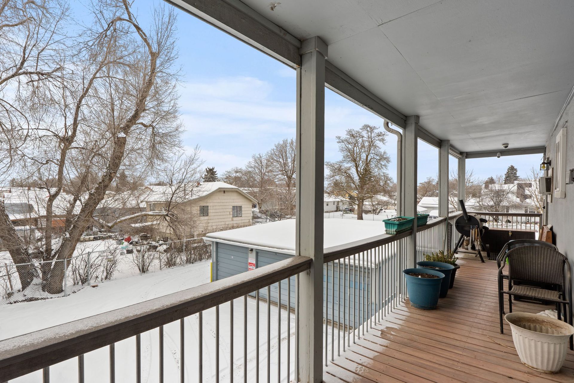 View from a covered balcony overlooking a snow-covered neighborhood with houses and trees under a cloudy sky.