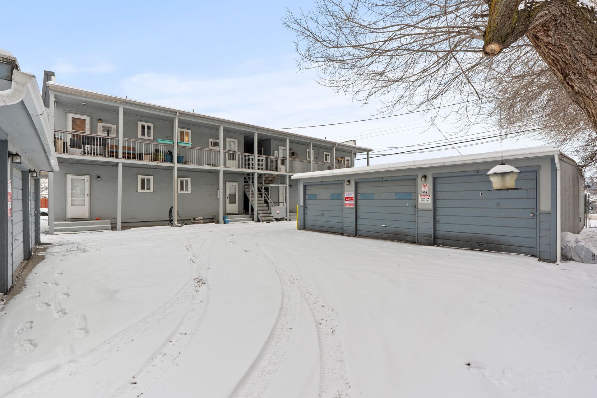 Snowy apartment building with garages. Gray exterior, balconies, and a snow-covered parking area.