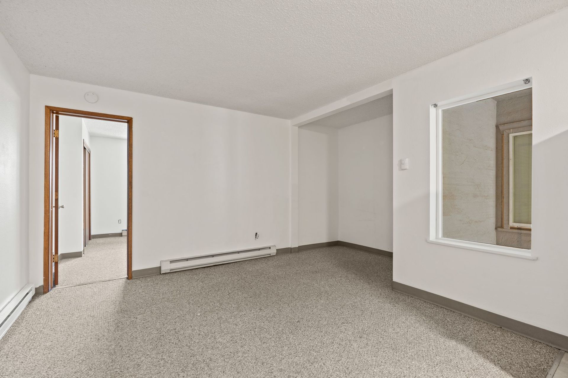 Empty, white-walled room with a doorway, window, and speckled flooring.