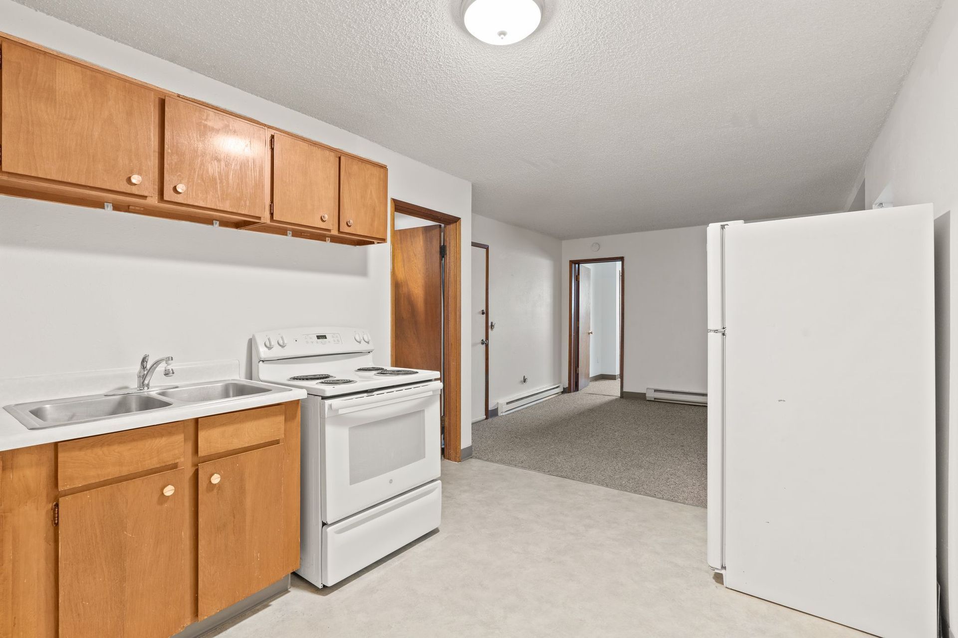 Kitchen with white appliances, light wood cabinets, and doorway to a carpeted room.