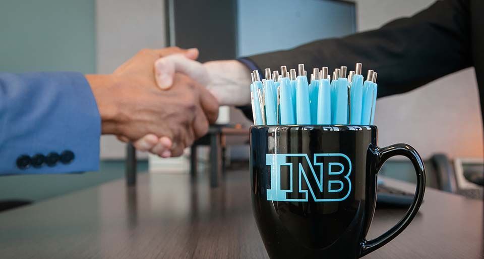 Two people shaking hands beside a black mug holding blue pens on a conference table