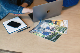 Desk with a laptop, notebook, smartphone, pen, and two magazines on a wooden table