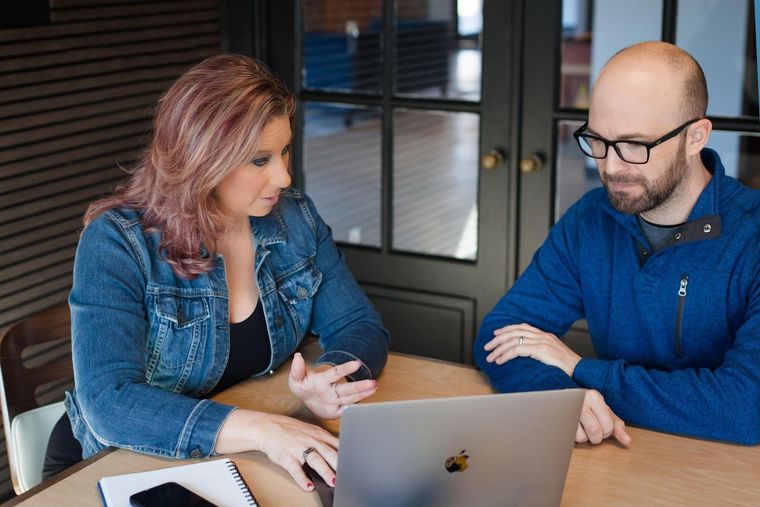 Two colleagues discussing over a laptop at a table in an office setting