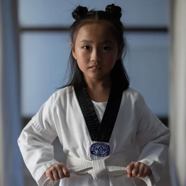 A young girl is wearing a white karate uniform with a black belt