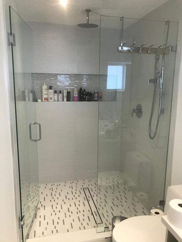 Glass-enclosed shower with white and black tiled floor, built-in shelf with toiletries.