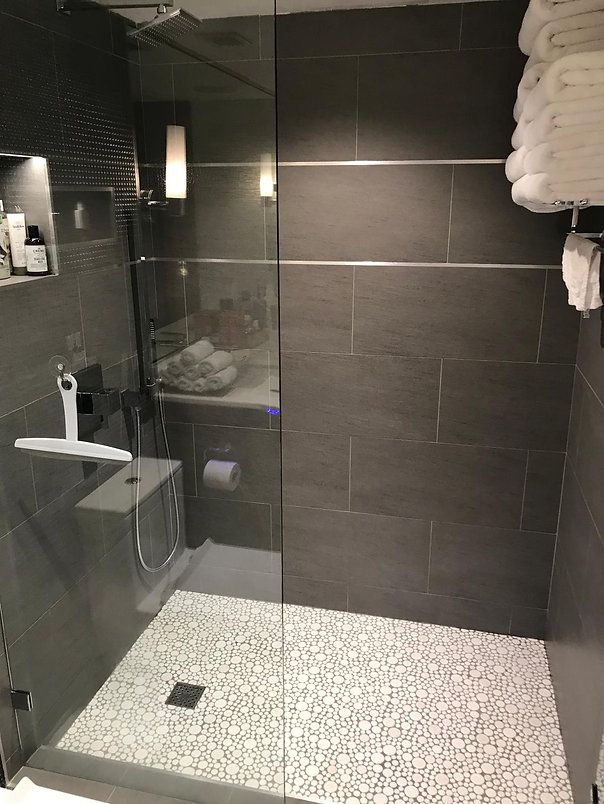 Modern shower with pebble floor, gray tile walls, glass door, and white towels.