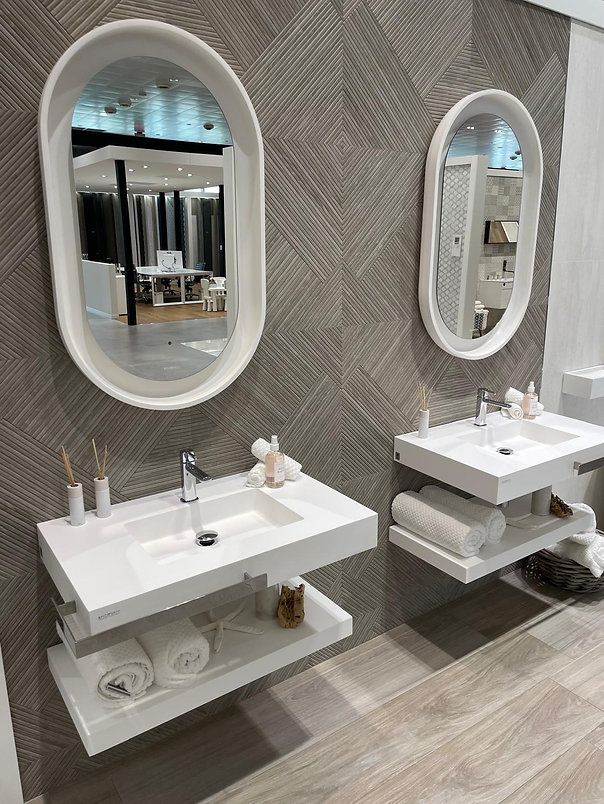 Two white floating bathroom sinks with shelves and oval mirrors on a gray textured wall.