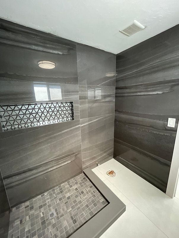 A modern gray tiled shower with a mosaic floor and built-in shelf.
