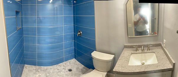 A modern bathroom with blue tiled shower, toilet, and a vanity with a mirror.