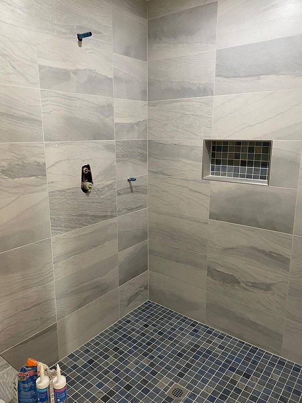 Tiled shower with blue and gray patterned floor, gray walls, and built-in niche. Plumbing fixtures visible.