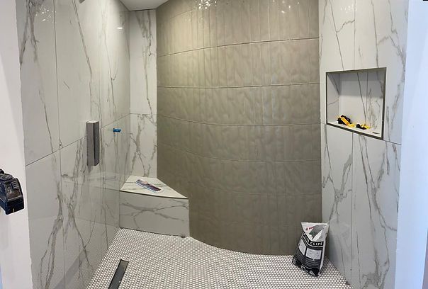 Modern shower stall with marble-look and beige tile walls, corner bench, and recessed shelf.
