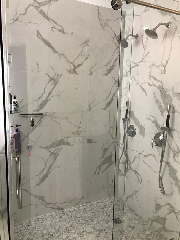 Shower with white marble-look tiles, glass doors, and pebble floor. Chrome fixtures.