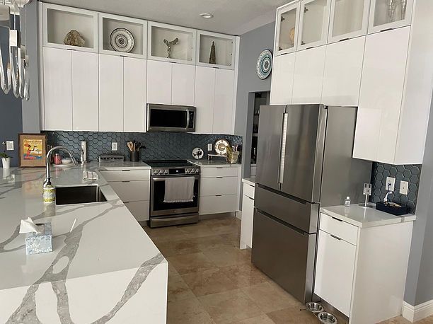 Modern white kitchen with stainless steel appliances, marble countertop island, and blue tile backsplash.