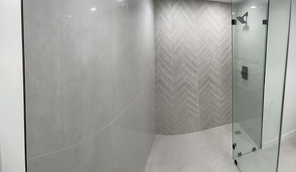 Modern shower with glass doors, gray and herringbone tile walls, and silver shower head.