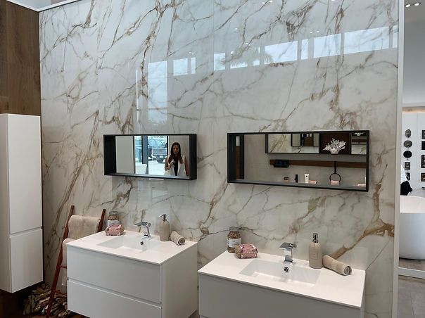 Bathroom with marble walls, two white vanities, and rectangular mirrors.