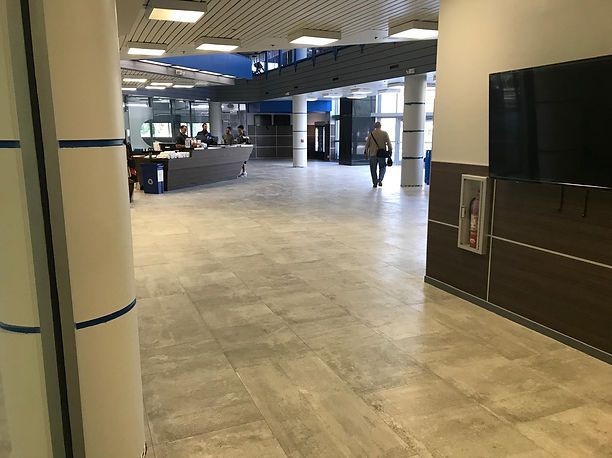 Spacious lobby with tiled floor, reception desk, and a person walking toward exit doors.