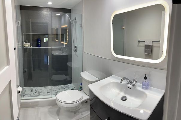 Modern bathroom with glass shower, toilet, vanity, and backlit mirror.