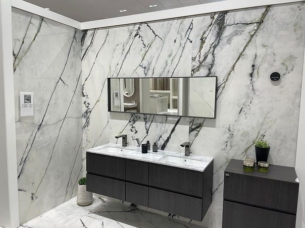 Bathroom with white marble walls and flooring, dark wood vanity, long mirror, and black fixtures.