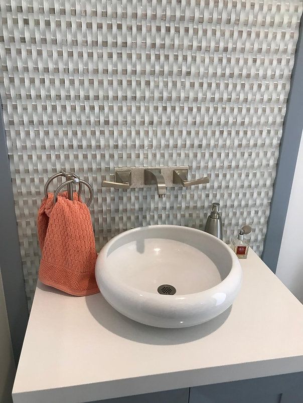 White round sink on a white countertop. Peach towel hangs. Textured gray tile backsplash.