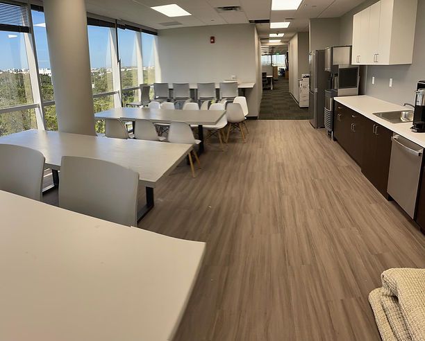 Office break room with tables, chairs, cabinets, sink, and appliances.