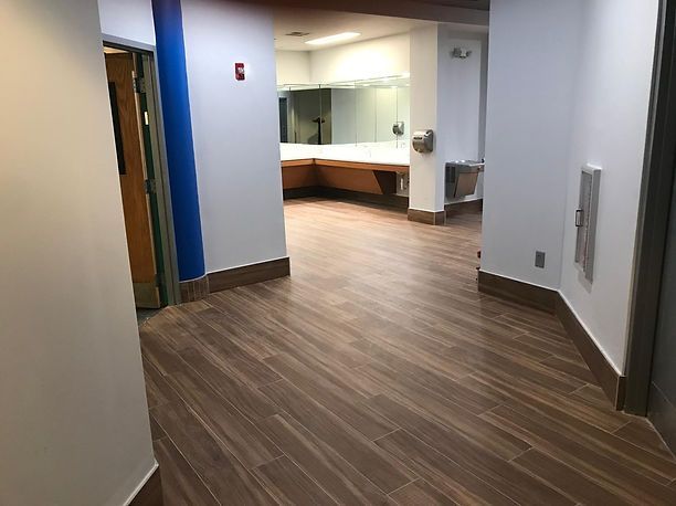 Hallway with wood-look flooring leads to a brightly lit room with a large mirror and counter space.