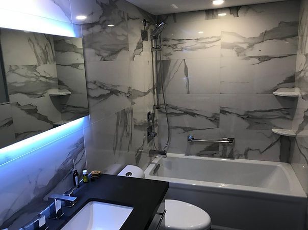 Modern bathroom with marble-patterned tile walls, bathtub, toilet, and sink with a mirror and led lighting.