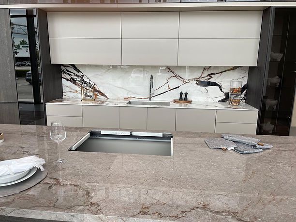 Modern kitchen with stone countertops and cabinetry; sink; patterned backsplash.