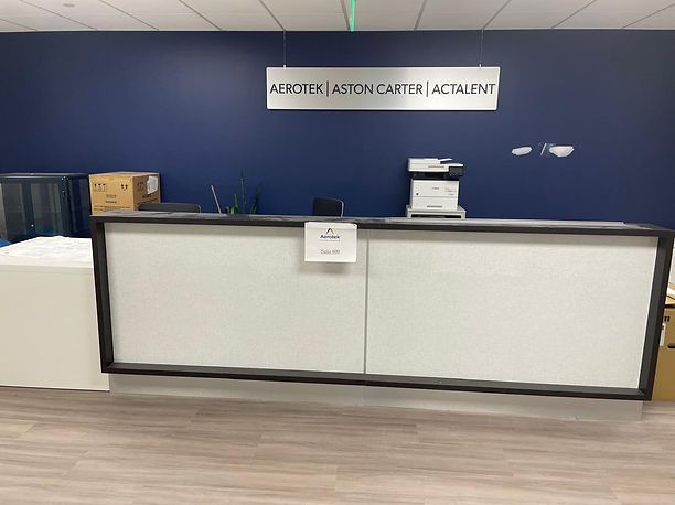 Reception desk with white front, black trim, and a blue wall above with company names.