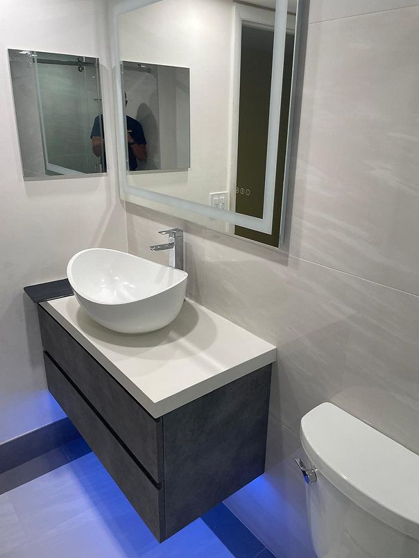 Modern bathroom with floating vanity, vessel sink, LED-lit mirror, and toilet. Gray and white color scheme.