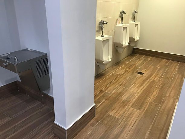 Public restroom with three urinals, water fountain, and wood-look flooring.