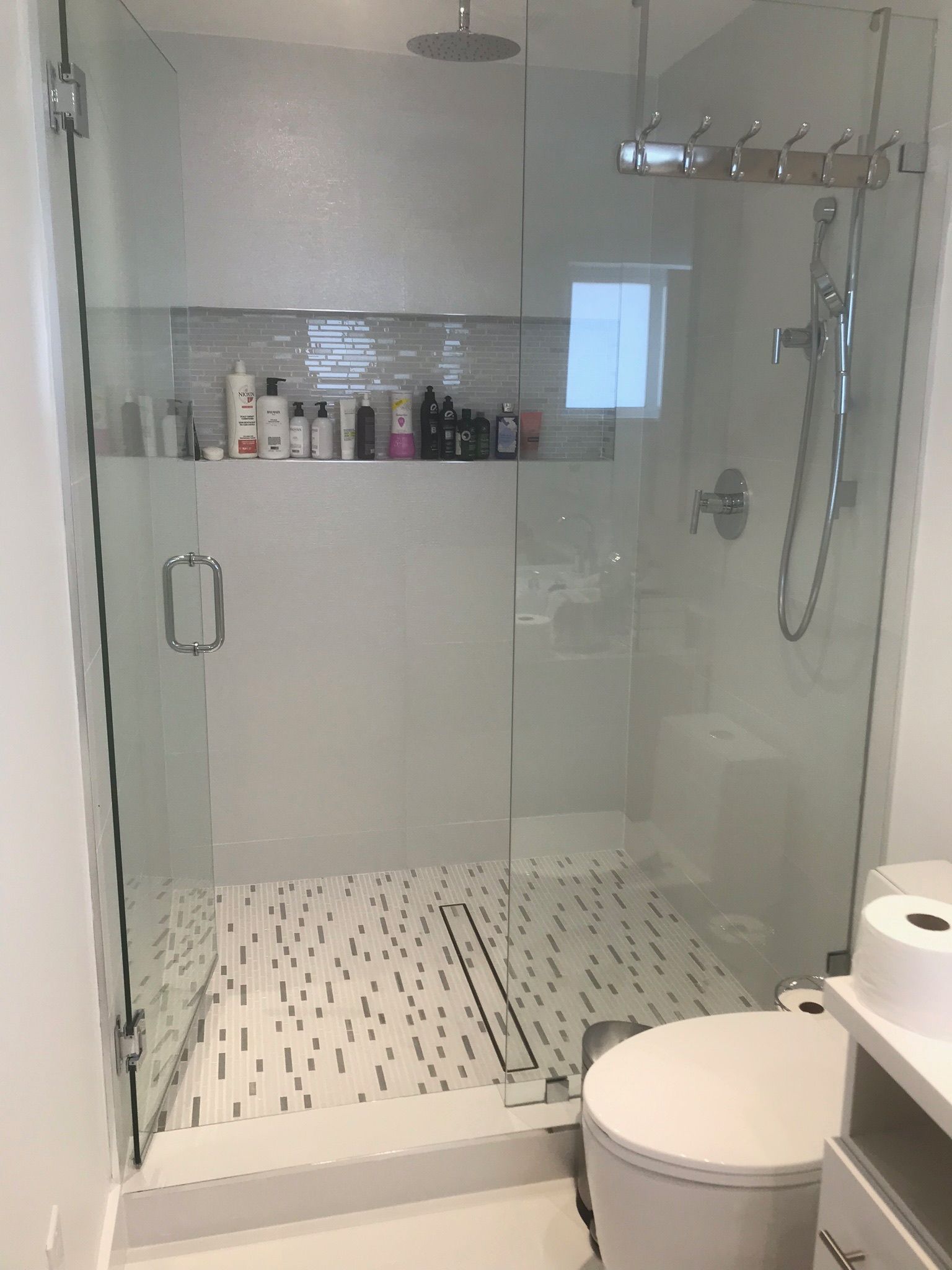 Modern bathroom with gray tile, toilet, sink, and window with blinds.