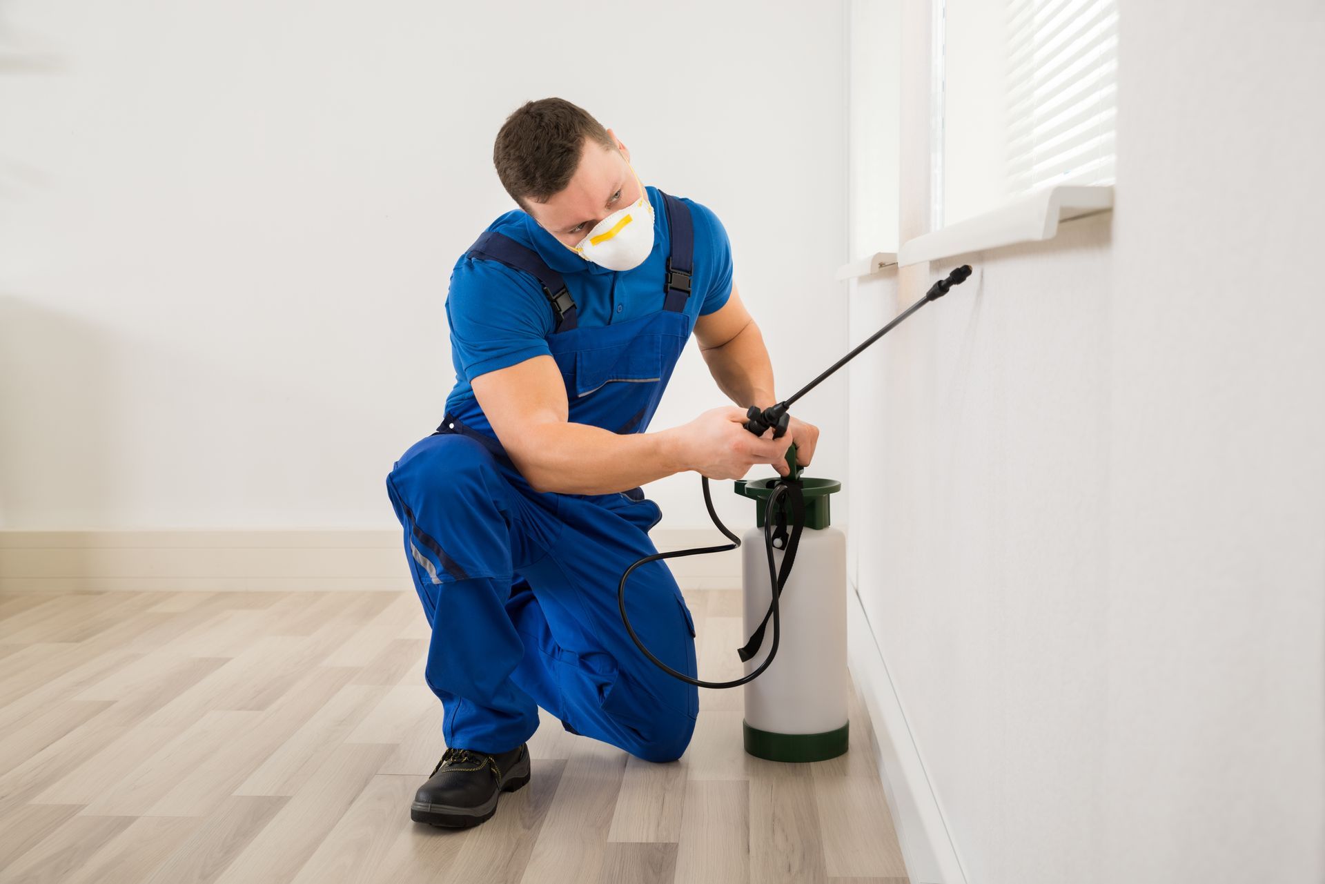 Exterminator spraying baseboard with sprayer for pest control services inside residential home.