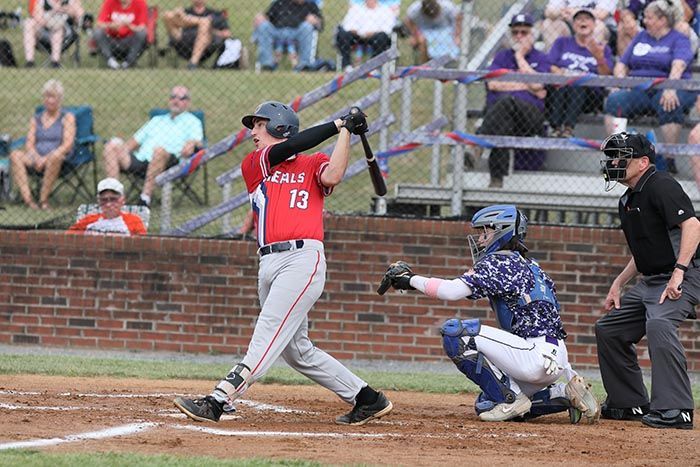 A baseball player is swinging a bat at a pitch while a catcher watches.