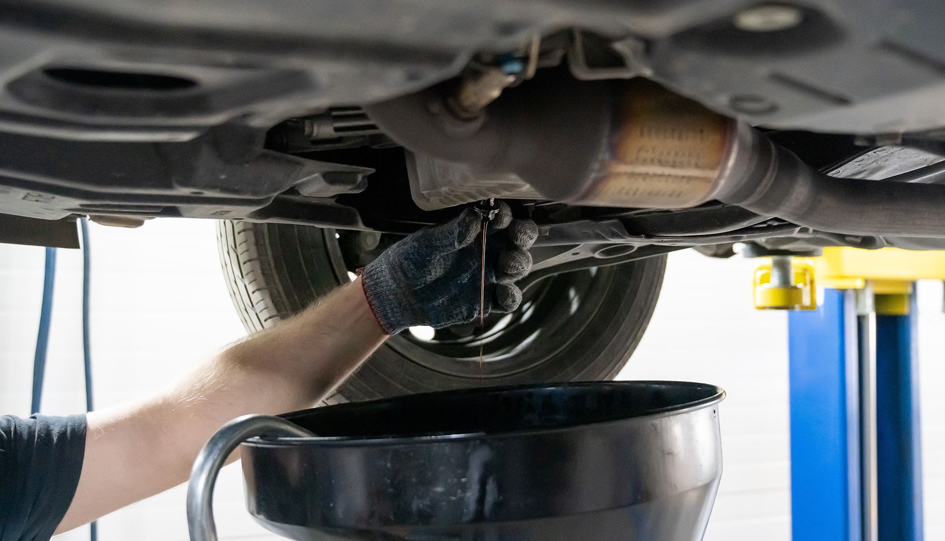 Mechanic draining oil from a car, holding a wrench over a drain pan, viewed from below.