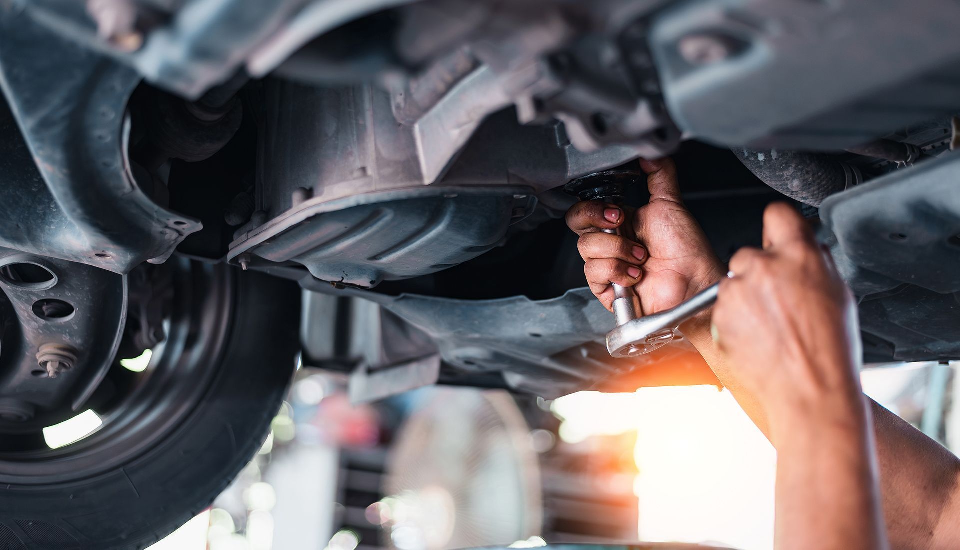 Person working on the underside of a car with a wrench.