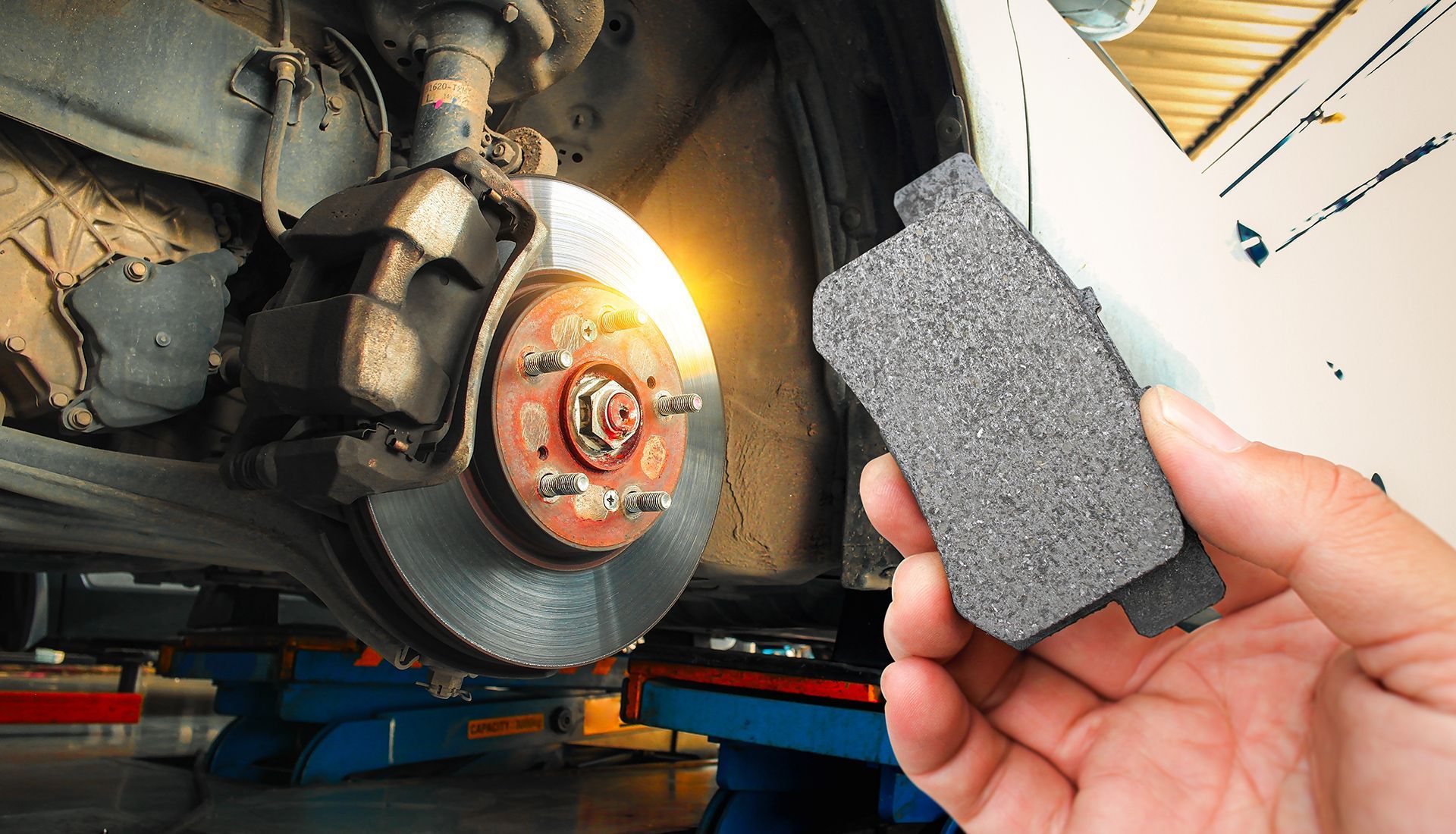 Hand holding new brake pad, car's brake disc visible, garage setting.