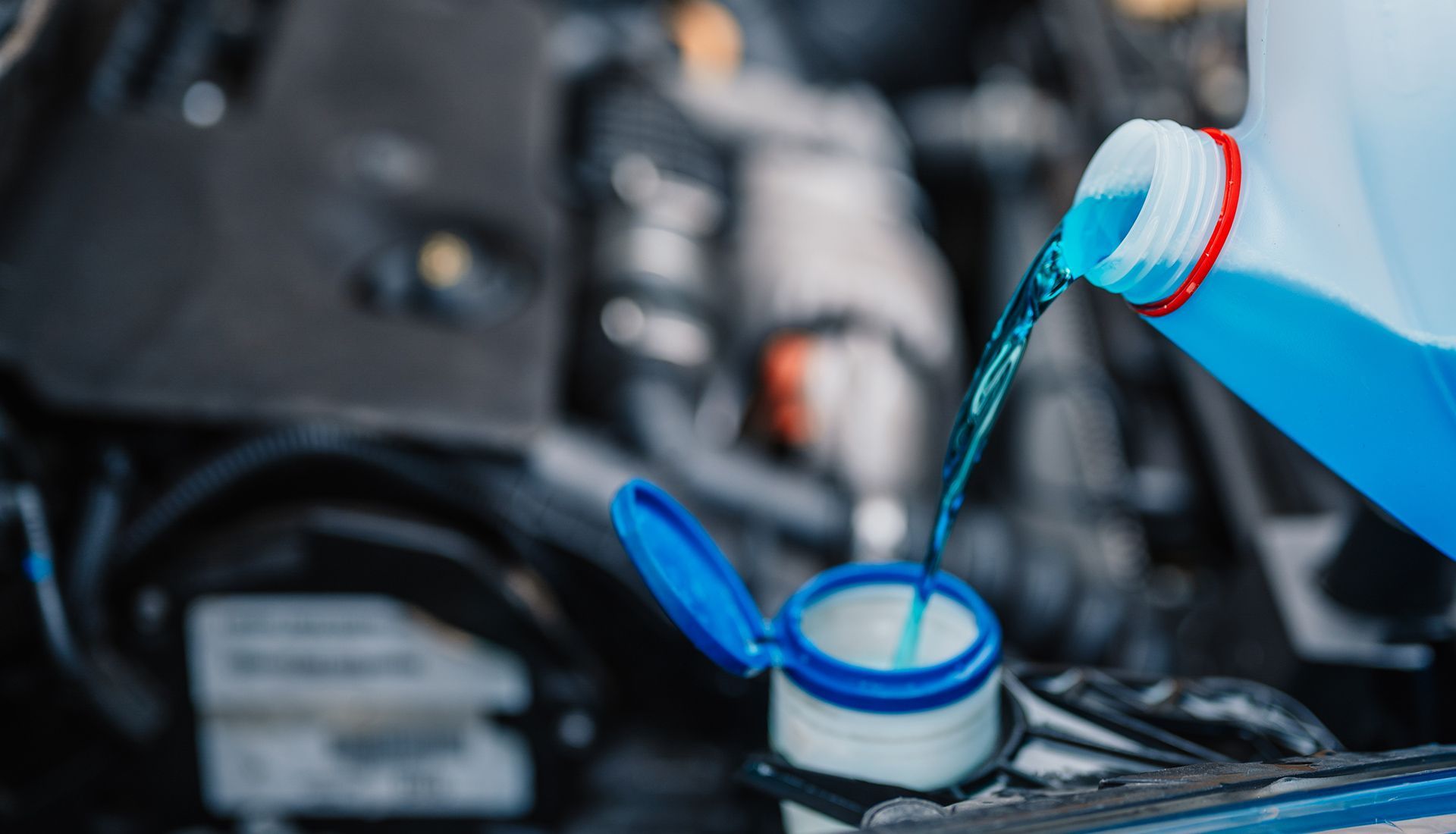 Blue windshield washer fluid being poured into a car's reservoir under the hood.