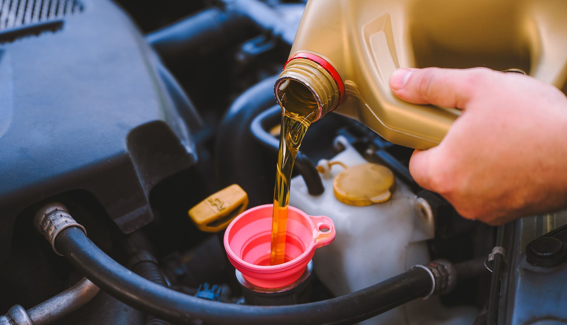 Person pouring motor oil into a car engine with a funnel.