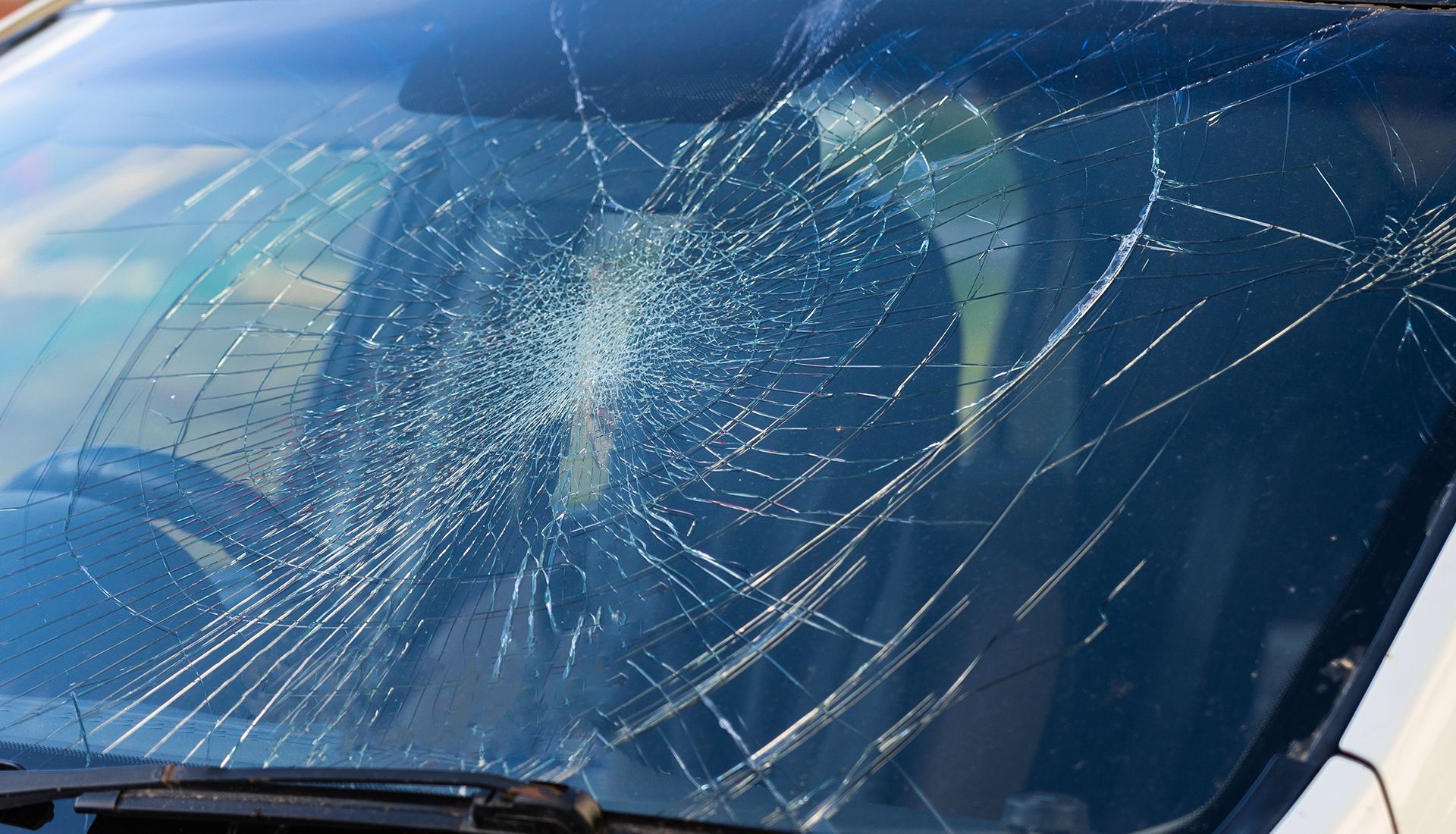 Shattered car windshield with spiderweb-like cracks across the glass; visible interior, black wiper blades.
