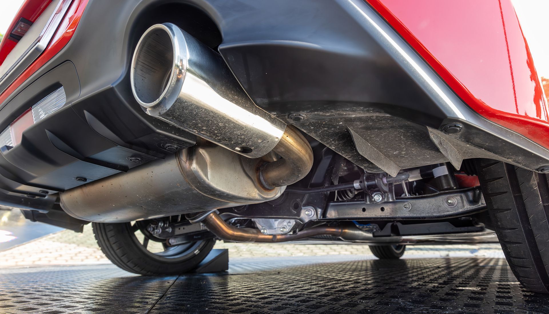 Undercarriage of a red car, showing exhaust pipe, muffler, and suspension parts.