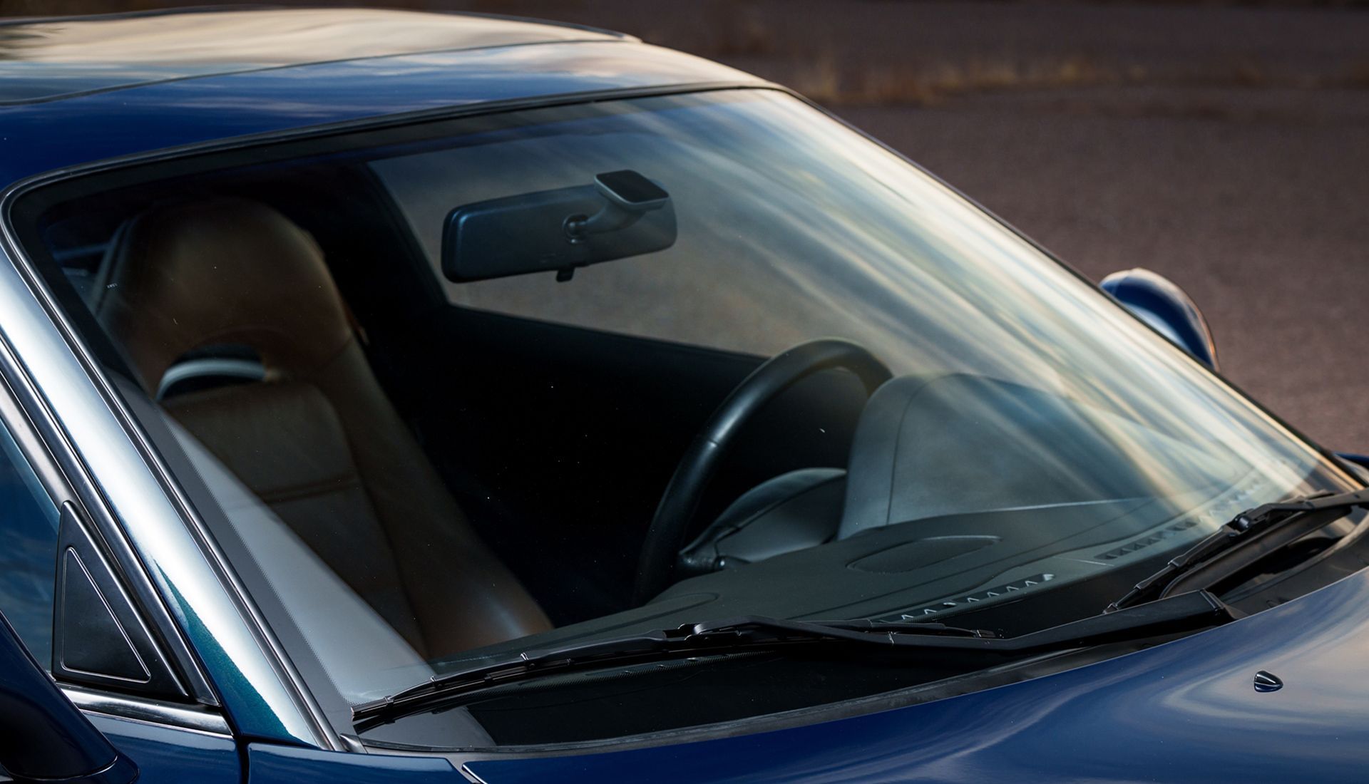 Blue car interior with brown leather seat, steering wheel, and rearview mirror.
