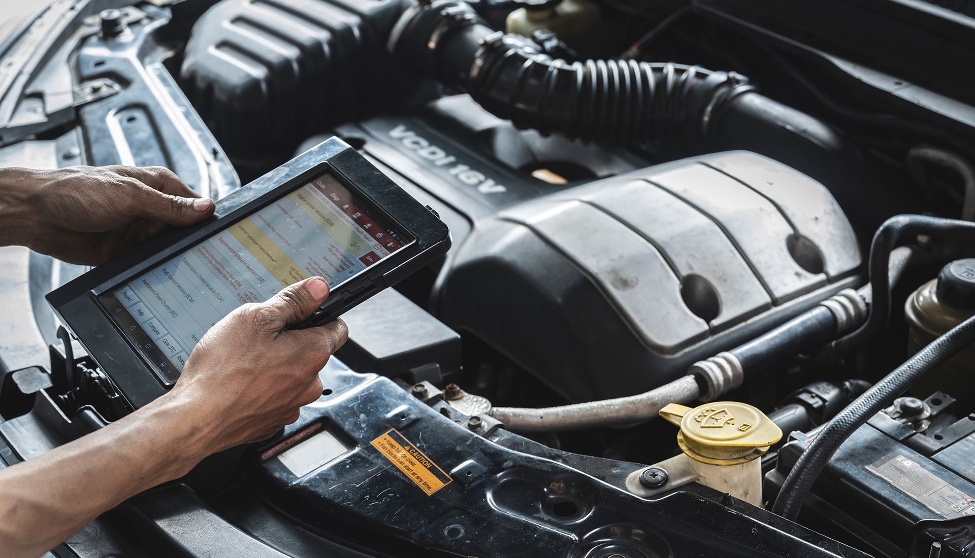 Mechanic using a tablet diagnostic tool on a car engine.